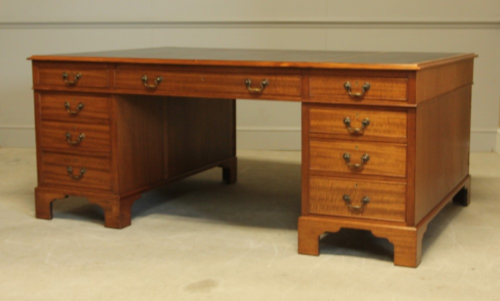 An early 20th-century mahogany partners desk featuring a dark leather writing surface, multiple drawers with brass swan-neck handles, and twin pedestals on bracket feet. View VI