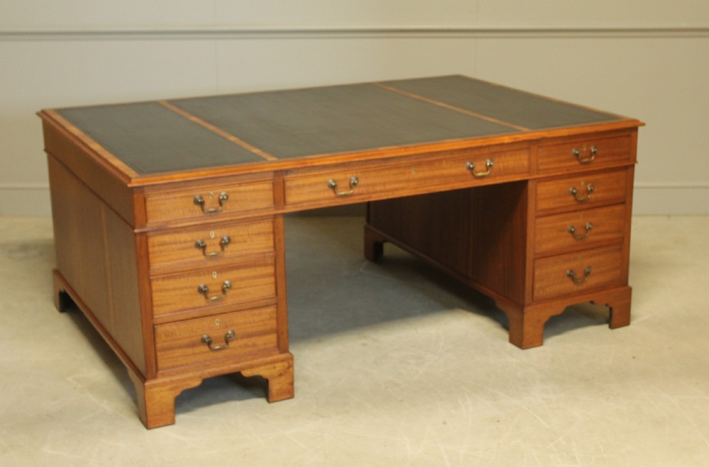An early 20th-century mahogany partners desk featuring a dark leather writing surface, multiple drawers with brass swan-neck handles, and twin pedestals on bracket feet. View VII