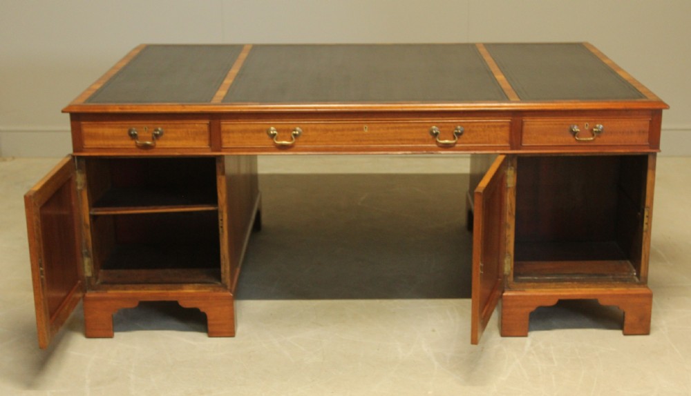 An early 20th-century mahogany partners desk featuring a dark leather writing surface, multiple drawers with brass swan-neck handles, and twin pedestals on bracket feet. View VIII