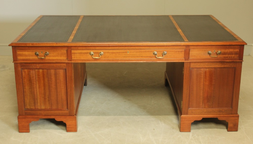 An early 20th-century mahogany partners desk featuring a dark leather writing surface, multiple drawers with brass swan-neck handles, and twin pedestals on bracket feet. View IX
