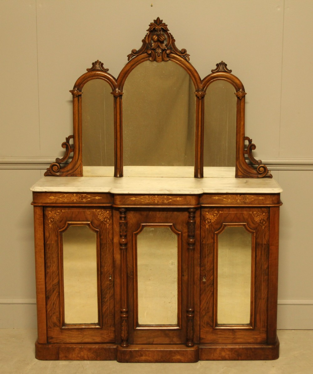 A Victorian burr walnut credenza with a white marble top, arched tri-fold mirror back, and three mirrored cabinet doors below.