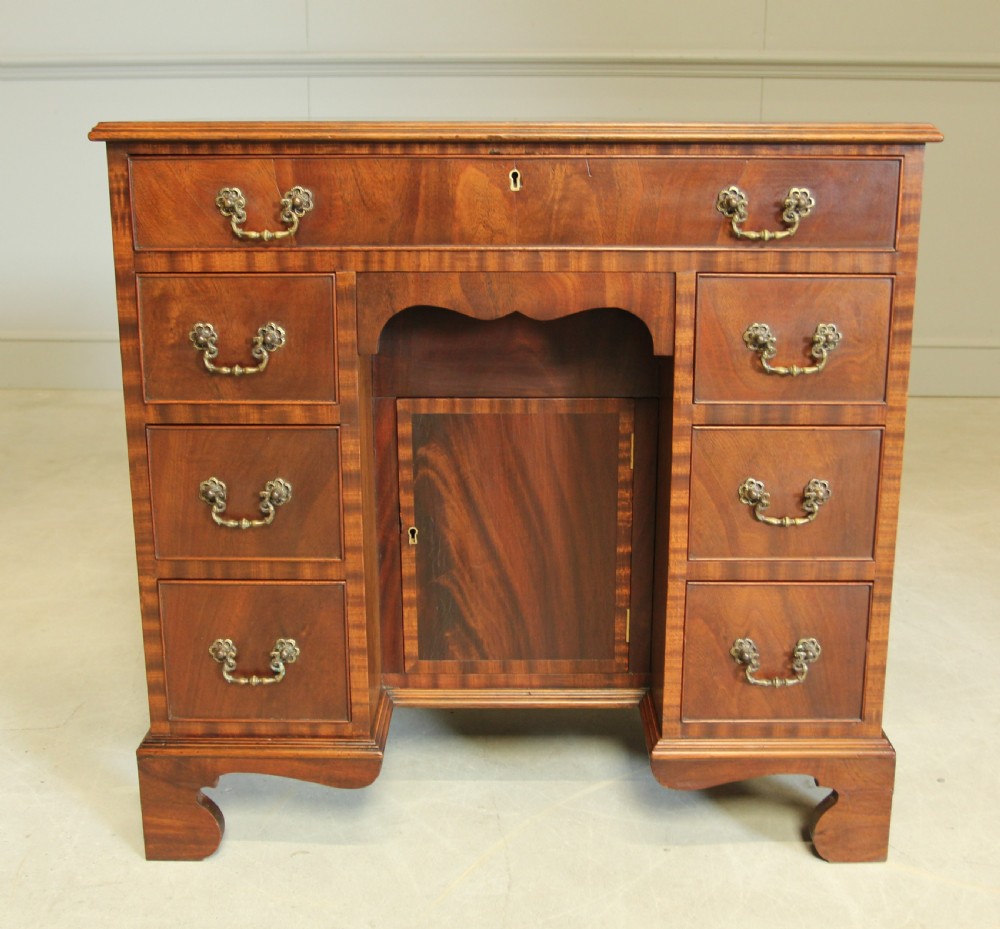 An early 20th-century mahogany kneehole desk featuring seven drawers with brass handles, a central recessed cupboard, and bracket feet. View II
