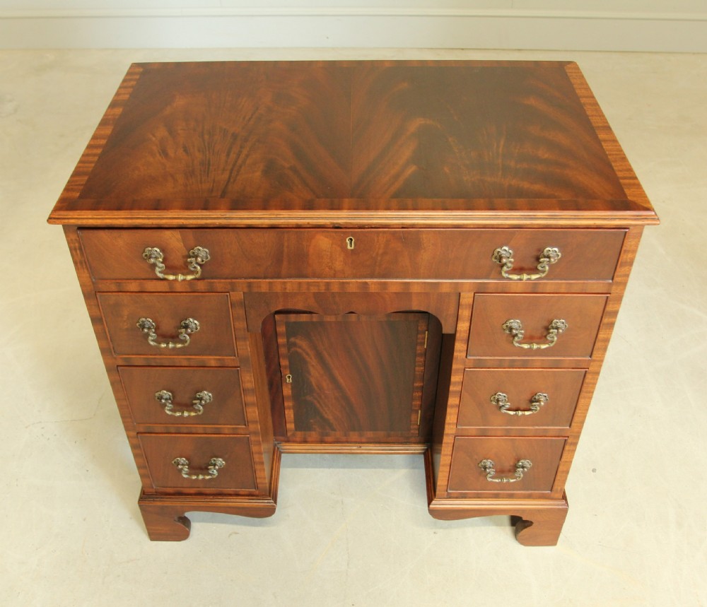 An early 20th-century mahogany kneehole desk featuring seven drawers with brass handles, a central recessed cupboard, and bracket feet. View III
