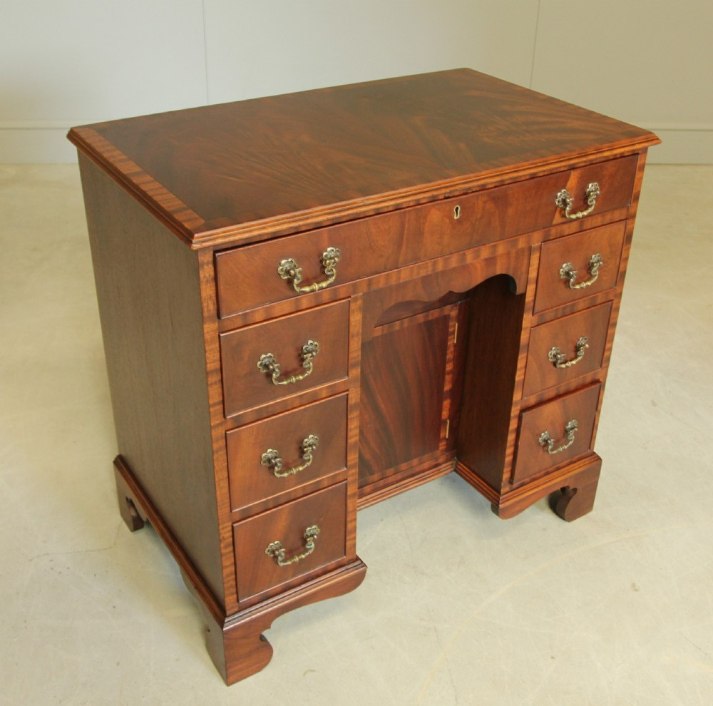 An early 20th-century mahogany kneehole desk featuring seven drawers with brass handles, a central recessed cupboard, and bracket feet. View V