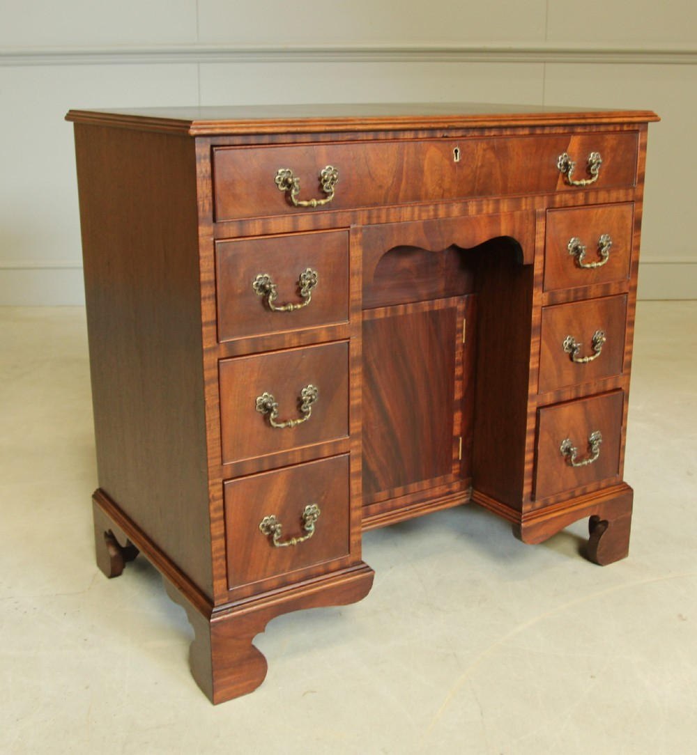 An early 20th-century mahogany kneehole desk featuring seven drawers with brass handles, a central recessed cupboard, and bracket feet. View VI