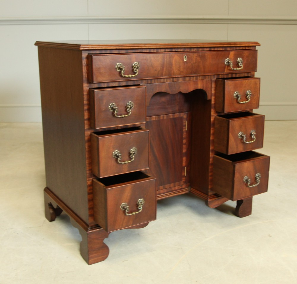 An early 20th-century mahogany kneehole desk featuring seven drawers with brass handles, a central recessed cupboard, and bracket feet. View VII