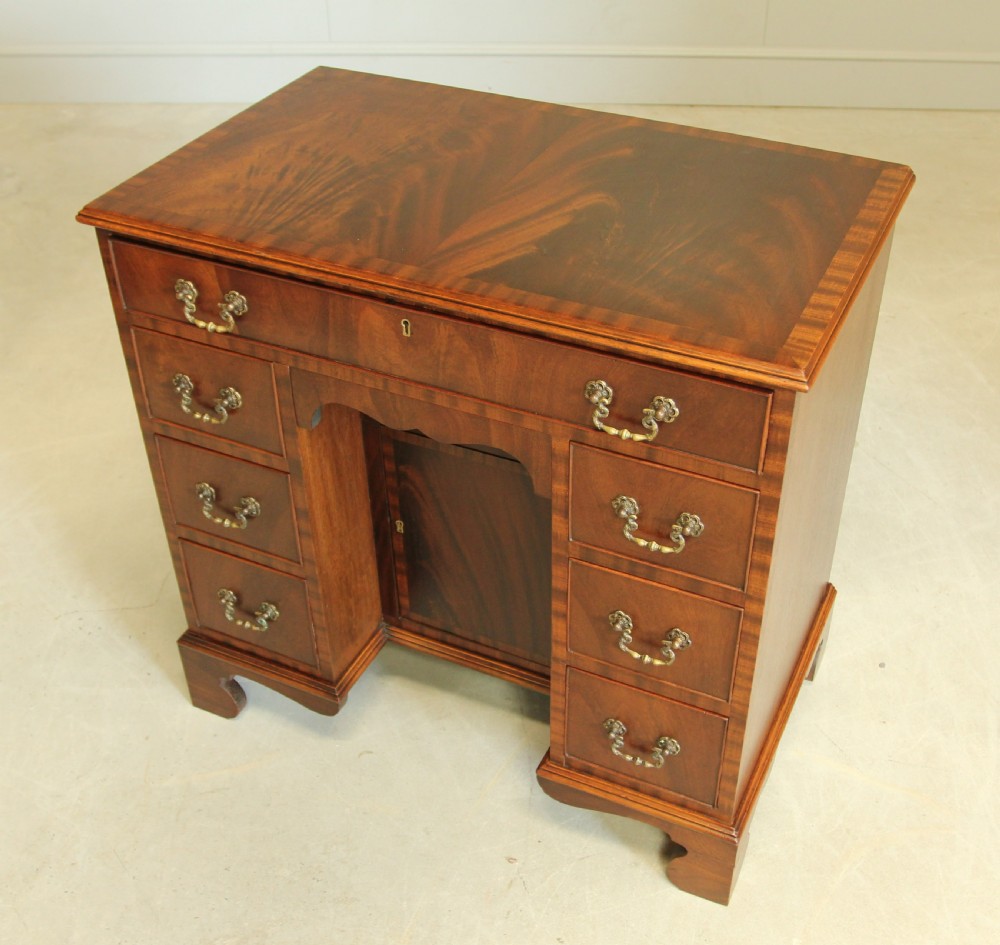 An early 20th-century mahogany kneehole desk featuring seven drawers with brass handles, a central recessed cupboard, and bracket feet. View VIII