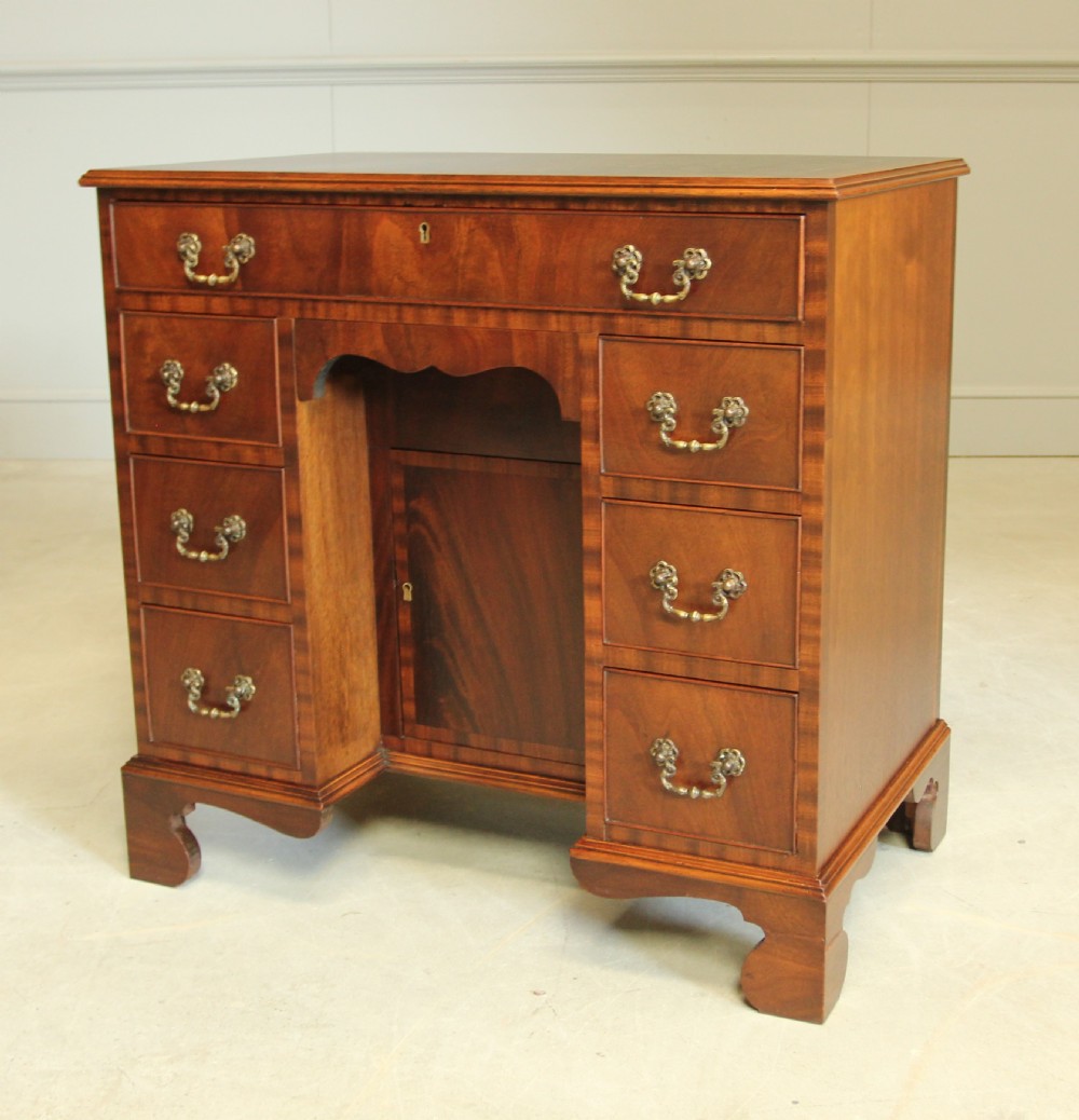 An early 20th-century mahogany kneehole desk featuring seven drawers with brass handles, a central recessed cupboard, and bracket feet. View IX