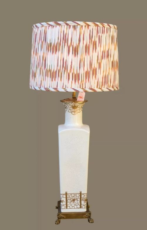 fig 1. A tall, square white porcelain table lamp with raised white floral motifs and gilt detailing, mounted on a brass claw-foot base.