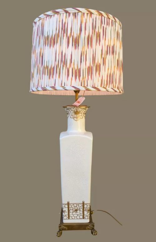 fig 2. A tall, square white porcelain table lamp with raised white floral motifs and gilt detailing, mounted on a brass claw-foot base.