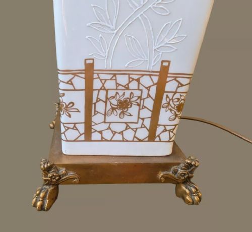 fig 3. A tall, square white porcelain table lamp with raised white floral motifs and gilt detailing, mounted on a brass claw-foot base.