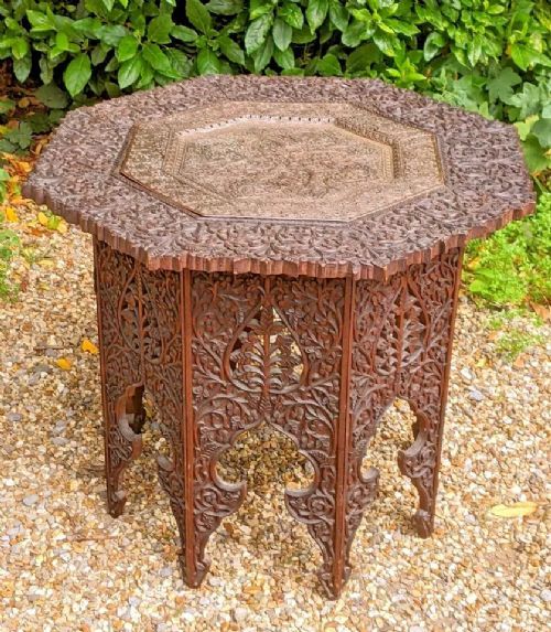 fig 1. An octagonal dark hardwood side table featuring intricate openwork floral carving and a central embossed copper top.