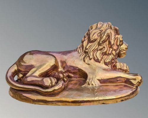 fig 1. A ceramic sculpture of a recumbent lion featuring a reflective copper lustre glaze resting on an integral oval base.