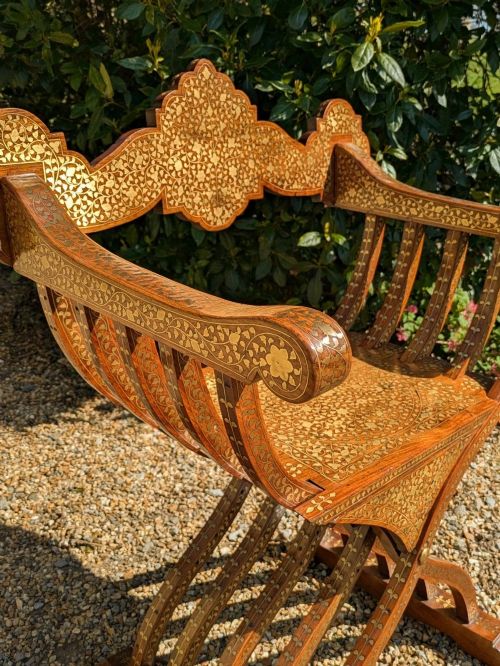 fig 1. A wooden X-frame Savonarola chair featuring detailed mother-of-pearl and bone geometric inlay across its slatted ribs, armrests, and decorative cresting.