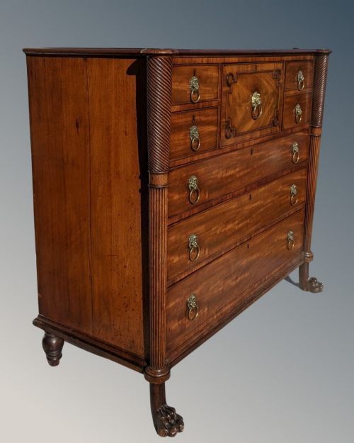 fig 1. A Regency mahogany chest of drawers featuring flame veneer drawer fronts, lion mask ring handles, spirally turned pilasters, and carved paw feet.