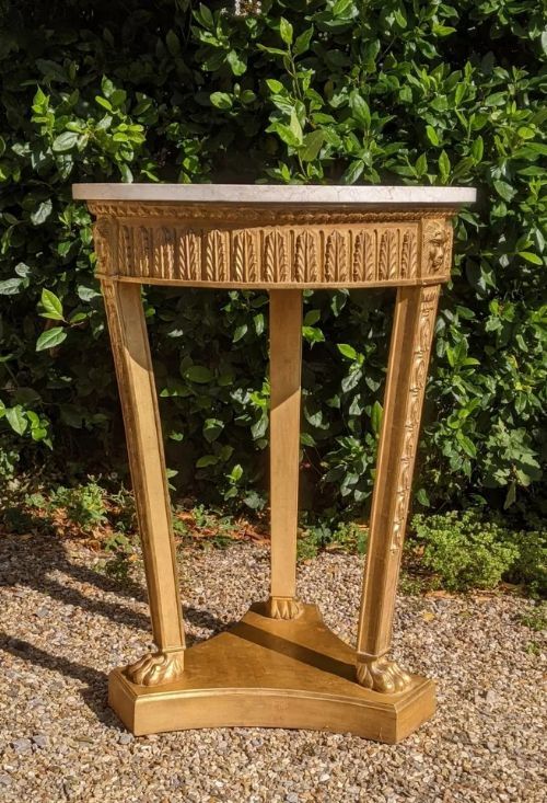 fig 1. A circular Regency style side table featuring a white marble top, carved giltwood frieze with lion head motifs, three tapered legs, and paw feet on a triform base.