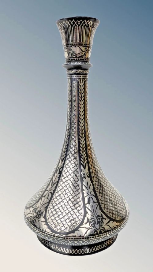 fig 2. An Indian Bidriware metal vase featuring a bulbous body, long neck, flared rim, and intricate silver inlay in floral and geometric patterns against a dark black ground.