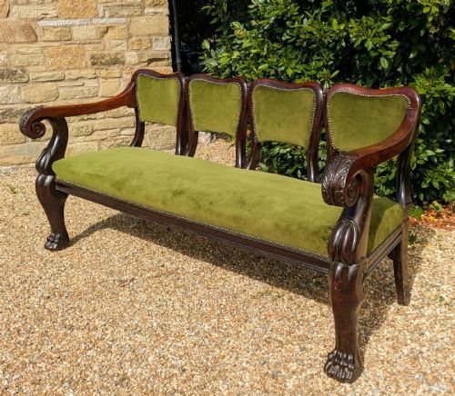 fig 1. An antique carved mahogany four-chair-back settle sofa upholstered in olive green velvet with brass stud detailing and carved paw feet.