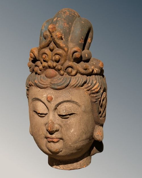 fig 1. A carved wooden head of a Buddhist deity featuring an ornate tall crown, serene facial features, and residual surface pigments.