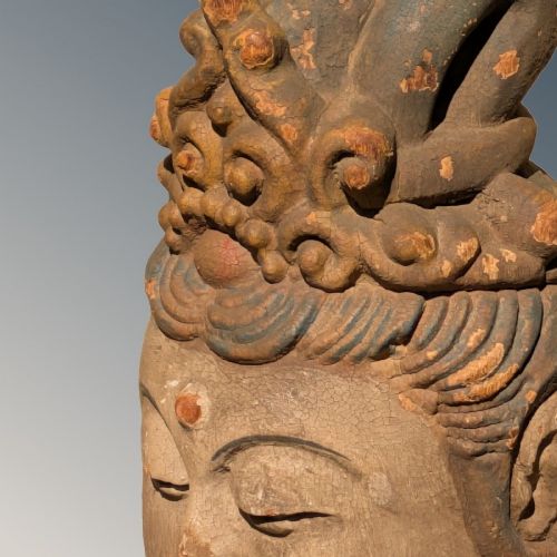 A carved wooden head of a Buddhist deity featuring an ornate tall crown, serene facial features, and residual surface pigments. View V