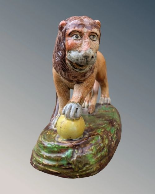 An early nineteenth-century Staffordshire pearlware lion figure featuring an ochre-tinted body with one paw resting on a yellow sphere, set upon a moulded green and brown glaze base. View III