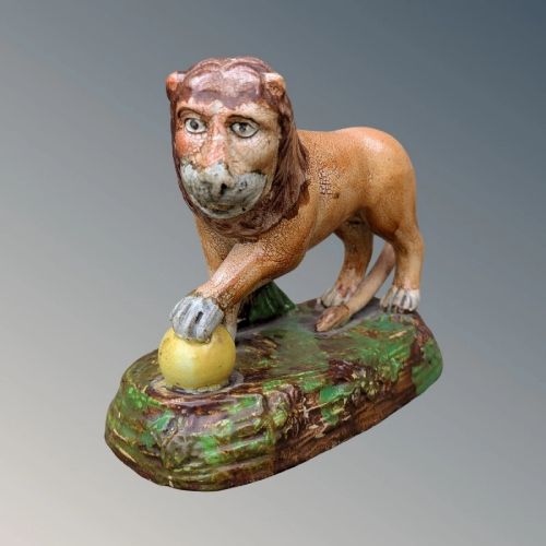 An early nineteenth-century Staffordshire pearlware lion figure featuring an ochre-tinted body with one paw resting on a yellow sphere, set upon a moulded green and brown glaze base. View IV