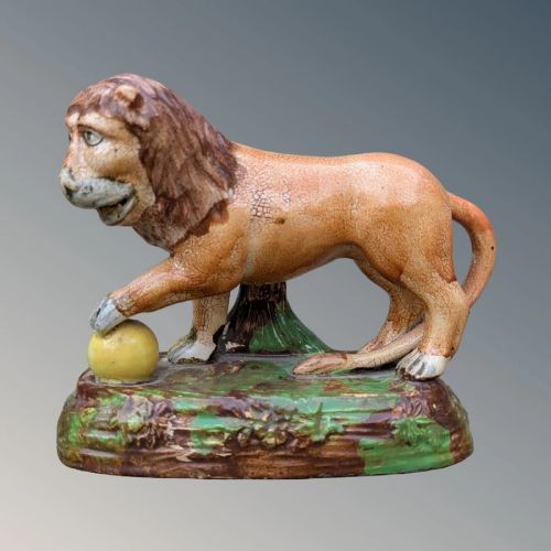 An early nineteenth-century Staffordshire pearlware lion figure featuring an ochre-tinted body with one paw resting on a yellow sphere, set upon a moulded green and brown glaze base. View V