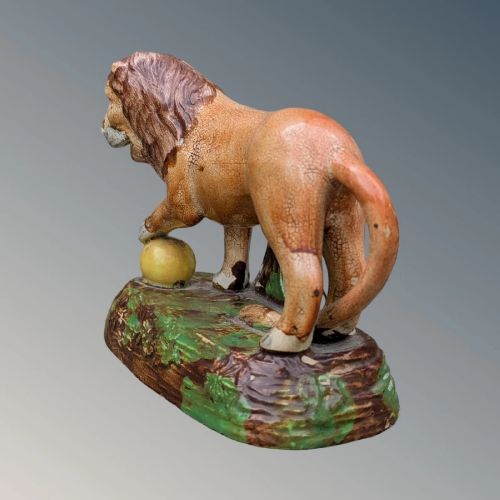 An early nineteenth-century Staffordshire pearlware lion figure featuring an ochre-tinted body with one paw resting on a yellow sphere, set upon a moulded green and brown glaze base. View VI