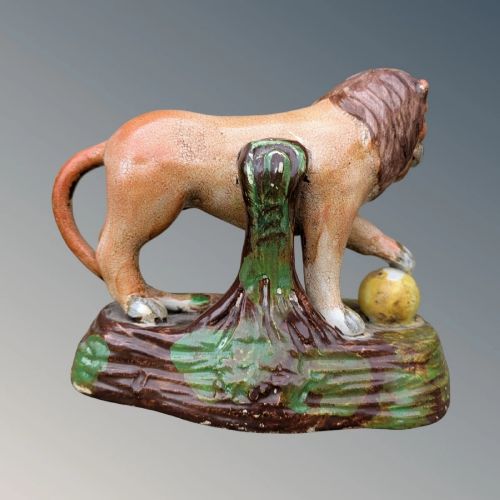 An early nineteenth-century Staffordshire pearlware lion figure featuring an ochre-tinted body with one paw resting on a yellow sphere, set upon a moulded green and brown glaze base. View VII