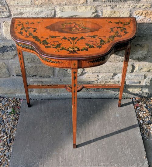 fig 1. A Regency satinwood demilune side table featuring hand-painted floral garlands and slender tapered legs.