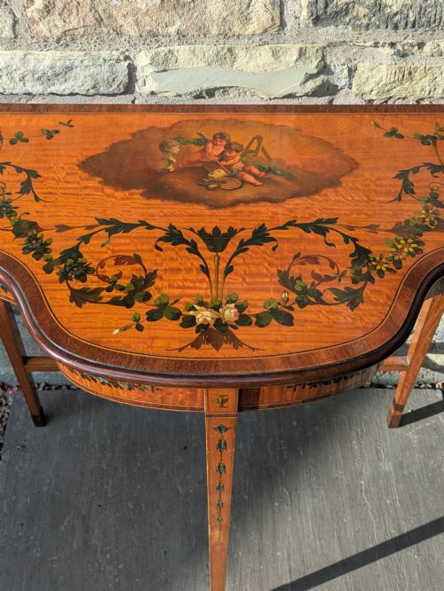 fig 2. A Regency satinwood demilune side table featuring hand-painted floral garlands and slender tapered legs.