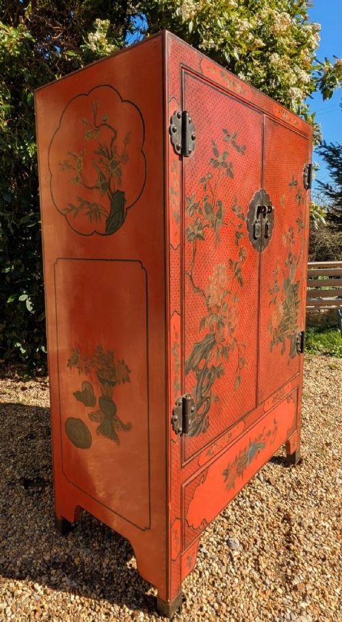 fig 1. A red lacquered two-door Chinese cabinet decorated with black and gold hand-painted floral and bird motifs, supported on straight block feet and fitted with brass hardware.