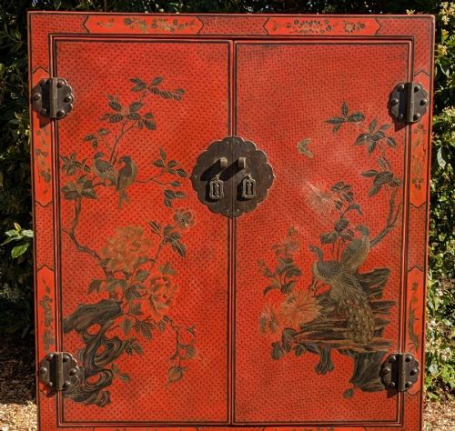 fig 3. A red lacquered two-door Chinese cabinet decorated with black and gold hand-painted floral and bird motifs, supported on straight block feet and fitted with brass hardware.