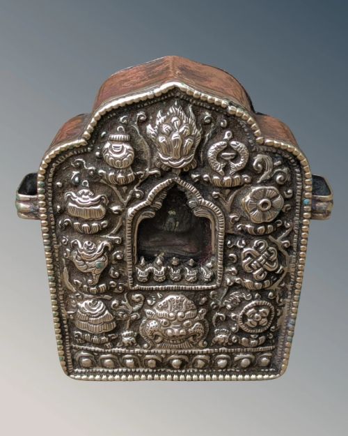 fig 1. An arched Tibetan Gau prayer shrine featuring an intricately embossed silver metal front panel mounted on a copper casing with side loops.