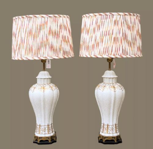 fig 1. A pair of white porcelain table lamps decorated with ornate gold leaf detailing, mounted on brass bases, and topped with cream pleated fabric lampshades.