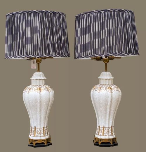 fig 2. A pair of white porcelain table lamps decorated with ornate gold leaf detailing, mounted on brass bases, and topped with cream pleated fabric lampshades.