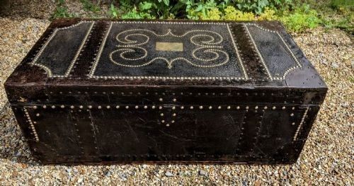 fig 4. A dark brown leather rectangular coffer decorated with brass stud patterns, scrolling motifs, and a central metal latch.