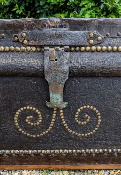 fig 5. A dark brown leather rectangular coffer decorated with brass stud patterns, scrolling motifs, and a central metal latch.
