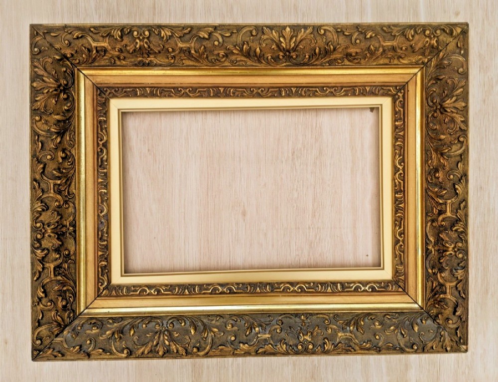 An ornate rectangular Victorian gilt picture frame featuring detailed foliage and scroll relief moulding around a stepped inner border.