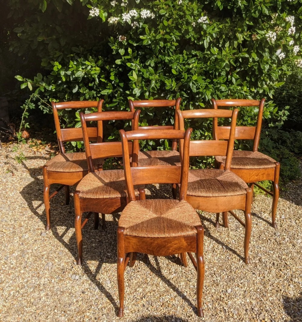 A set of six French provincial wooden dining chairs featuring woven natural rush seats, curved backrests, and front cabriole legs ending in carved hoof feet.