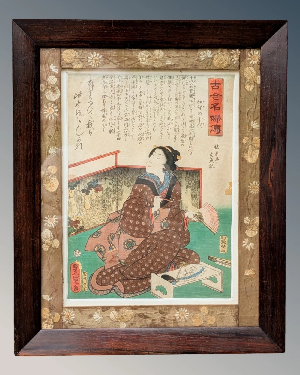 An antique Japanese ukiyo-e woodblock print depicting a seated female figure framed within a floral silk brocade border and a dark rosewood frame.