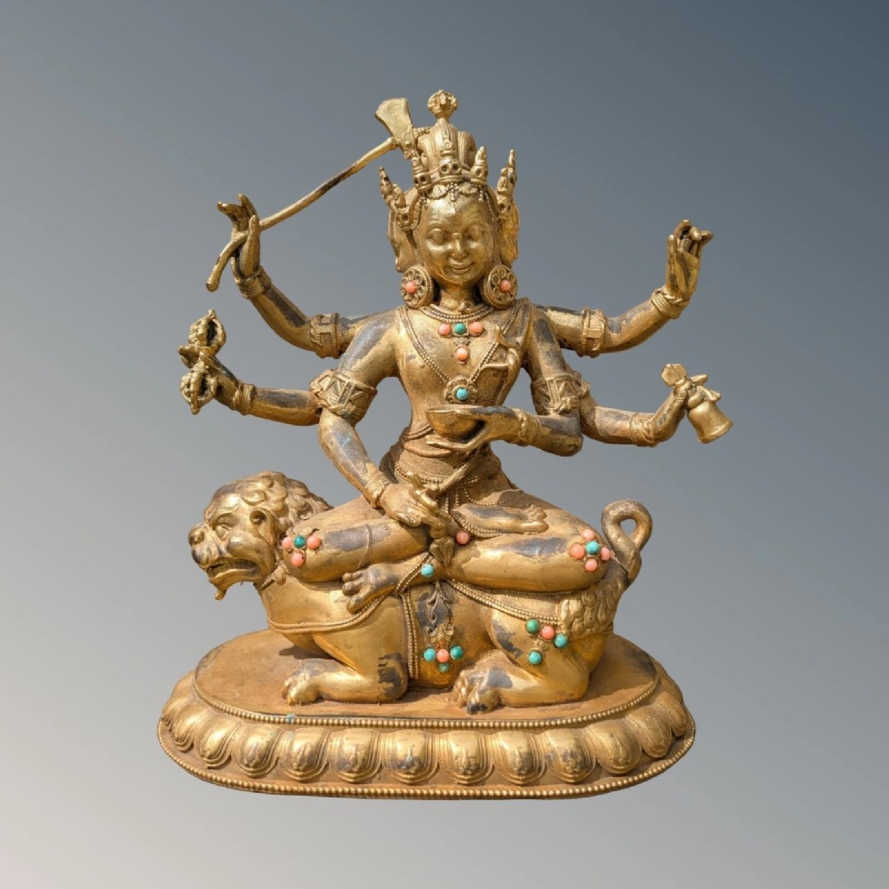 A gilt bronze multi-armed deity figure seated atop a lion mount with turquoise and coral bead ornamentation.