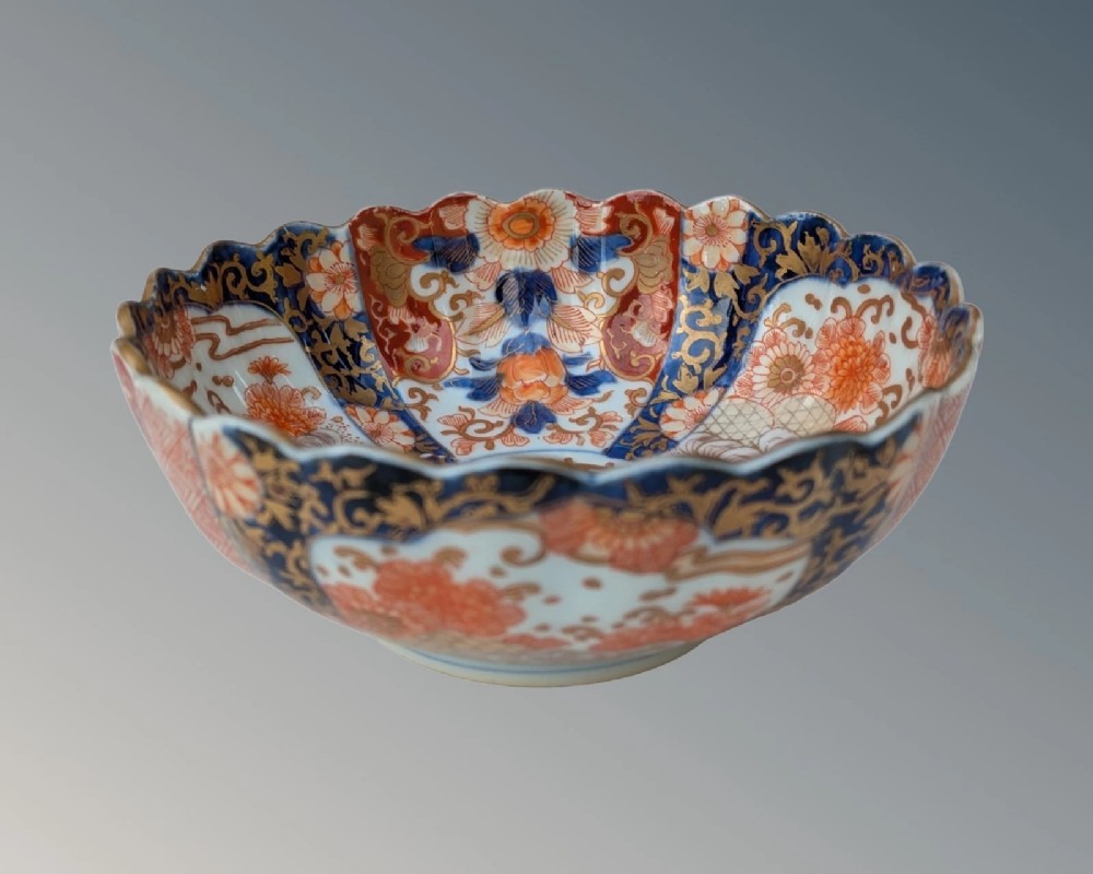 A Japanese Imari porcelain bowl with a scalloped edge, hand-painted in cobalt blue, rust red, and gold floral patterns.