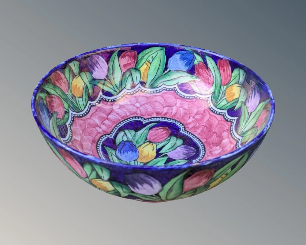 A circular Art Deco glazed earthenware bowl featuring hand-painted tulips in shades of purple, yellow, and red against a cobalt blue and pink background.