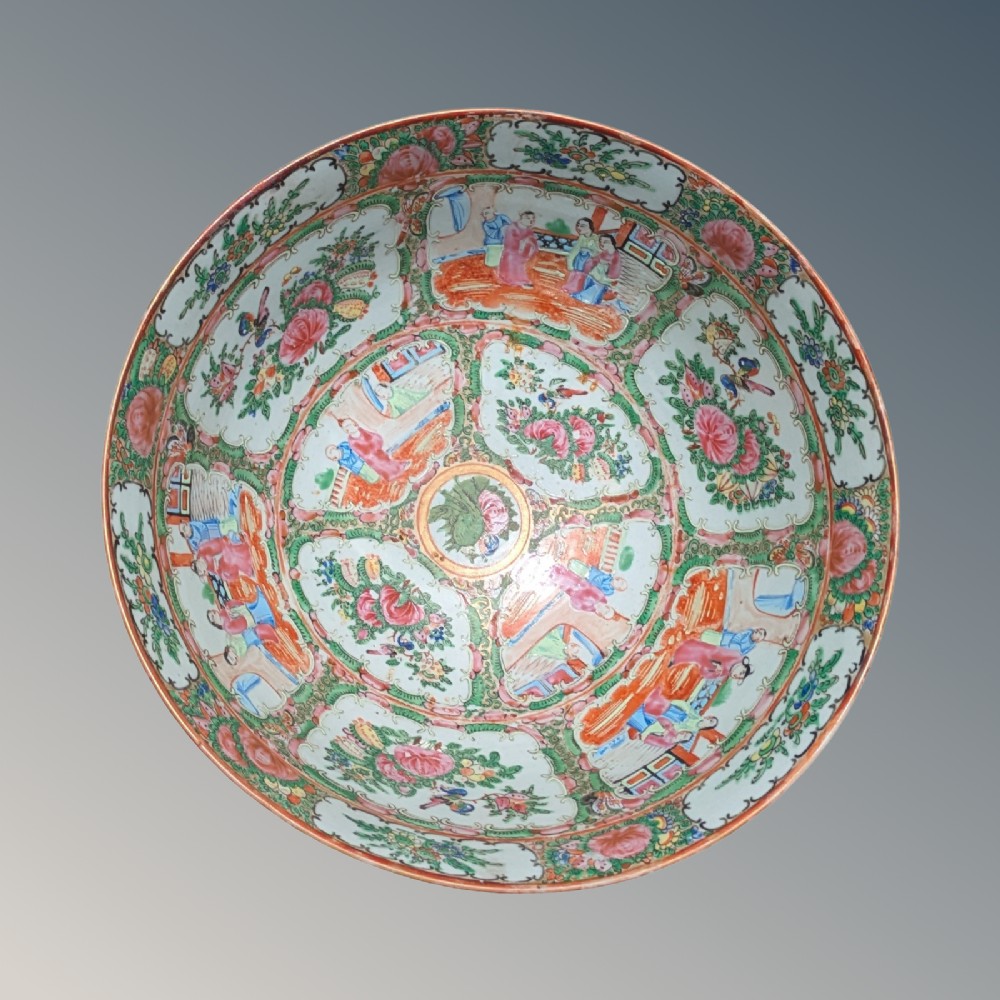 A top-down view of a circular 19th-century Chinese porcelain bowl featuring hand-painted Famille Rose enamels with alternating panels of figures and floral motifs.