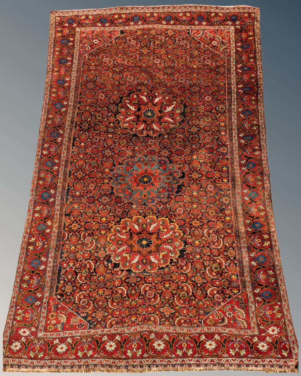 A rectangular hand-knotted Persian Khamseh carpet featuring three central floral medallions on a dense red patterned field with decorative borders.