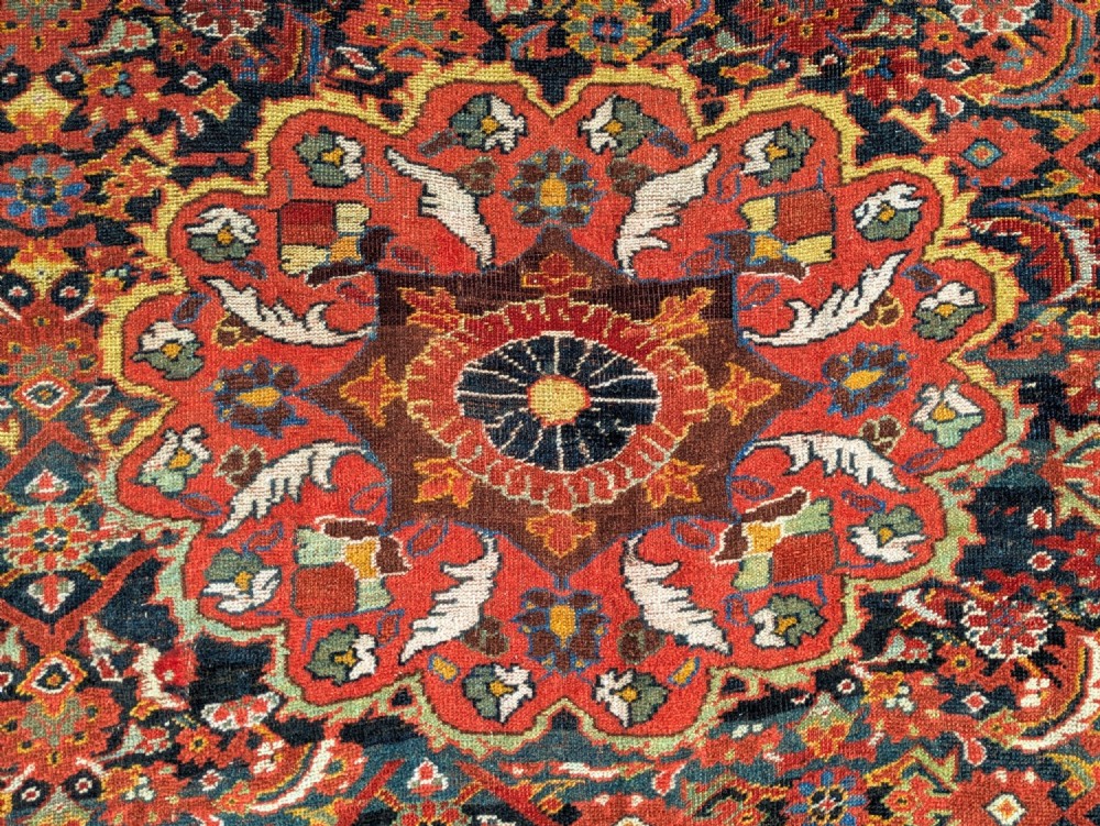 A rectangular hand-knotted Persian Khamseh carpet featuring three central floral medallions on a dense red patterned field with decorative borders. View III