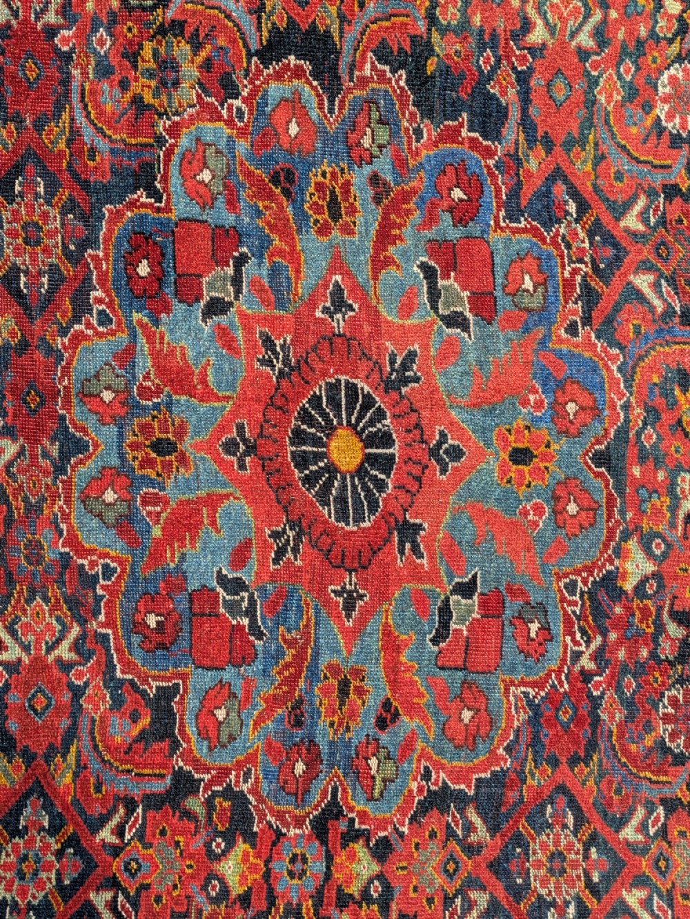 A rectangular hand-knotted Persian Khamseh carpet featuring three central floral medallions on a dense red patterned field with decorative borders. View IV