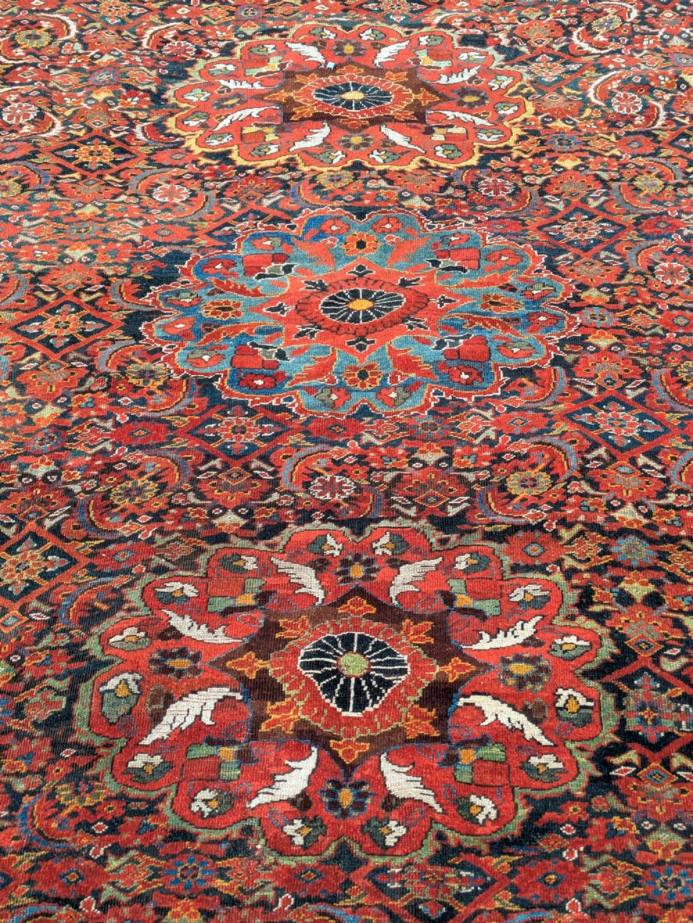 A rectangular hand-knotted Persian Khamseh carpet featuring three central floral medallions on a dense red patterned field with decorative borders. View V