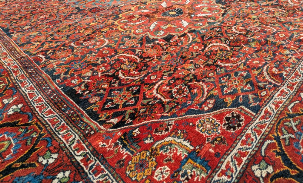 A rectangular hand-knotted Persian Khamseh carpet featuring three central floral medallions on a dense red patterned field with decorative borders. View VI
